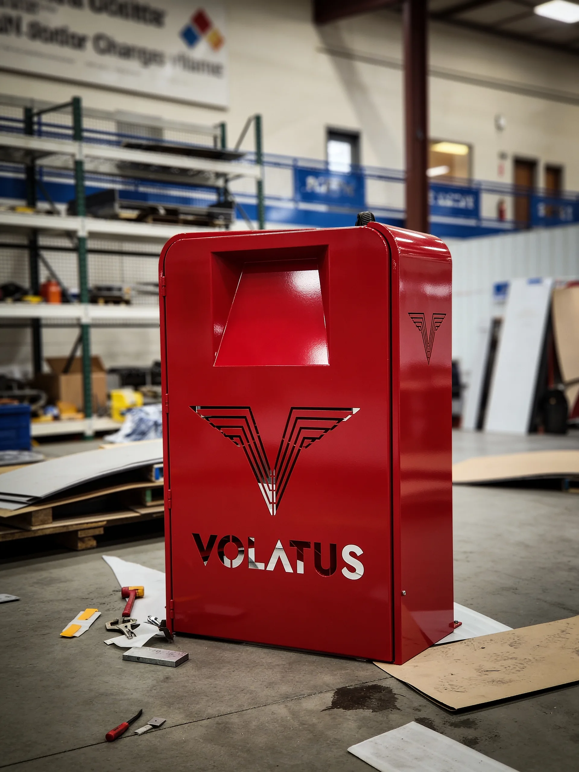 A completed red Volatus charger enclosure with the cut-steel V-chevron and wordmark, standing on the Wisconsin fabrication floor